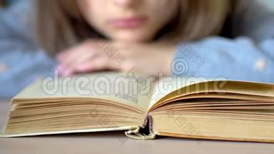 前景是一本书。 一个女孩在读一本书。 关闭视野。